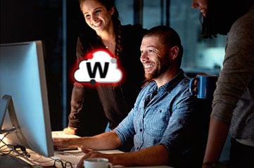 Smiling man surrounded by two female co-workers all looking at his monitor together