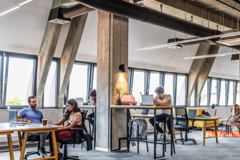 People sitting and standing in an open office space with high ceilings and industrial beams