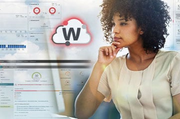 Black woman with natural curly hair in a white silk top looking at a monitor with WatchGuard Cloud screens behind her